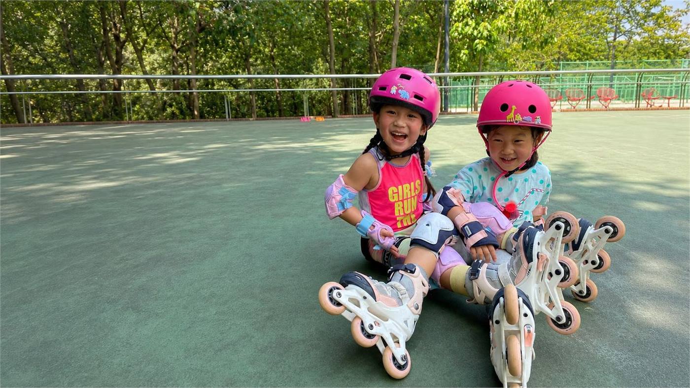兩位兒童和青少年穿著頭盔和滾軸溜冰鞋坐在戶外滾軸場地